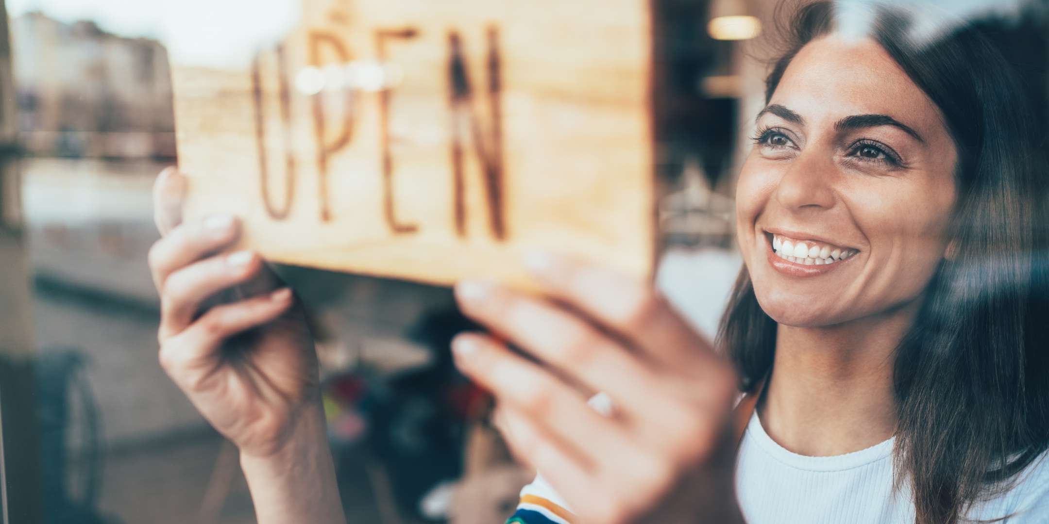 Portrait of a happy business owner hanging an open sign on the door at a cafe and smiling