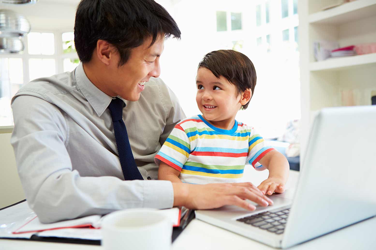 Busy Father Working Happily From Home With Son on his lap